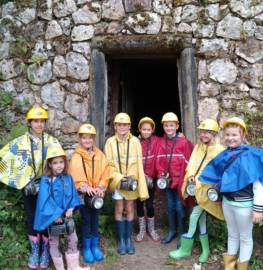 Kinder mit Helm, Grubenlampe und Poncho vor dem Stolleneingang des Bergwerks Silbergründle