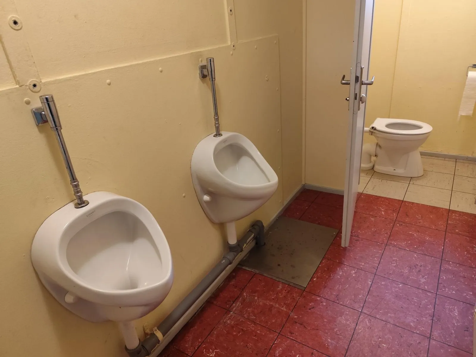 Toilettenraum im heutigen Clubhaus mit zwei Urinalen und einer Kabine, Boden und Wände sichtbar in die Jahre gekommen